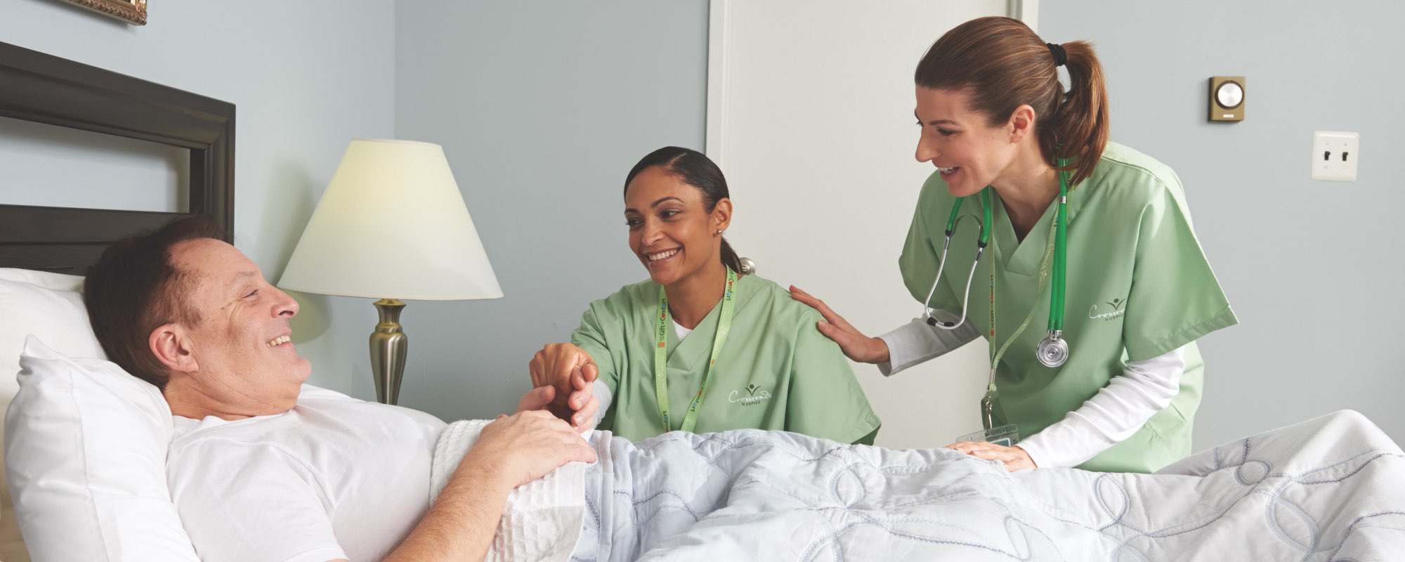 Two nurses at a patient’s bedside smiling
