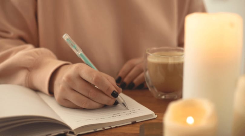 Person writing in a journal with a cup of coffee and candles