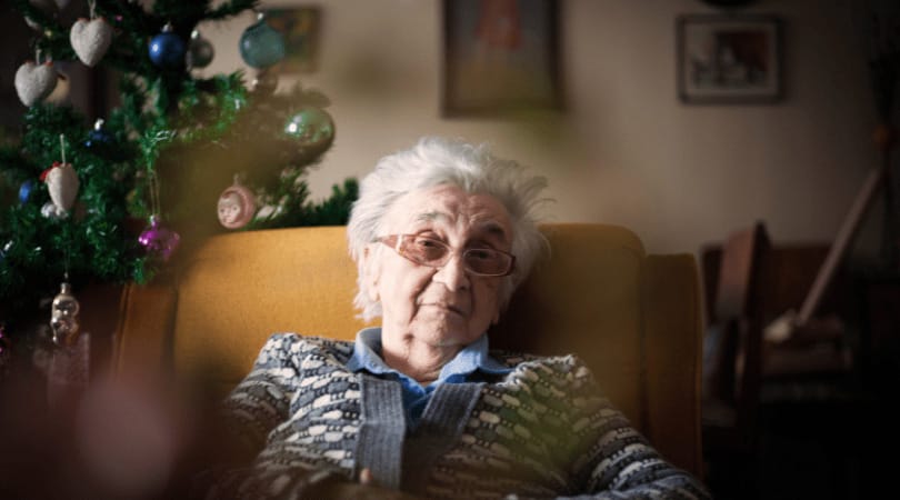 Elderly woman sitting in a chair by a Christmas tree