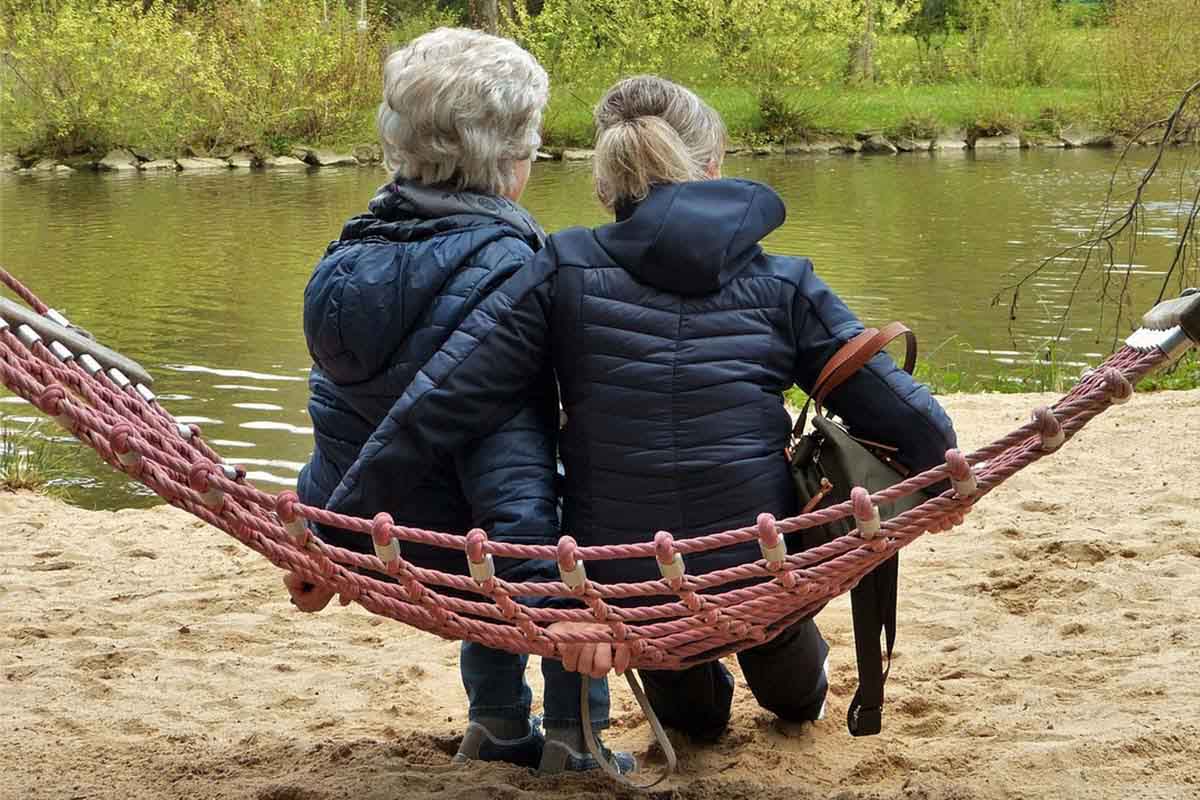 Two women sitting on a hammock by a lake
