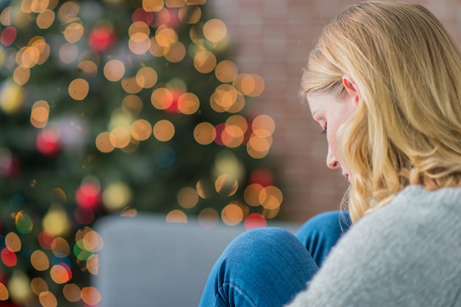 Blonde woman looking down by a Christmas tree)