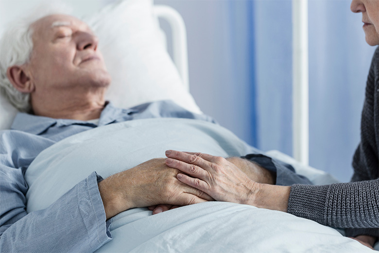 Terminal man in bed being comforted by a loved one